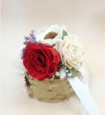 Preserved red rose and ivory flowers arranged in a natural birch wood vase with white ribbon