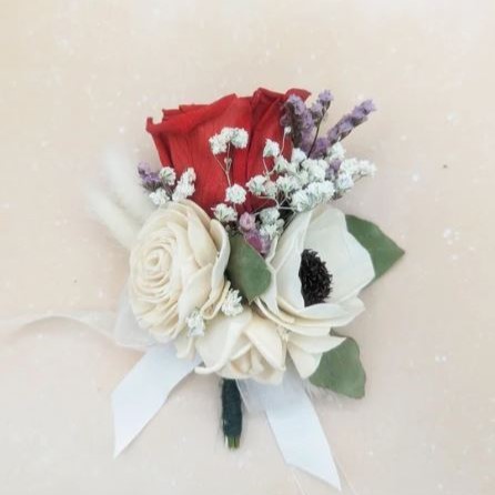 Red preserved rose boutonniere with ivory sola wood flowers, baby's breath, and lavender accents, tied with a white satin ribbon