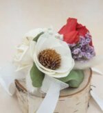 Preserved floral corsage with a red rose, white sola wood flower, cream rose, and purple accent flowers on a birch wood base with white ribbon