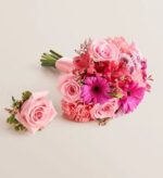 Matching pink prom bouquet and boutonniere set on a light background. The bouquet features pink roses, hot pink gerbera daisies, pink carnations, and alstroemeria wrapped with a pale pink ribbon. The boutonniere is a single pink rose with small accent flowers and greenery.