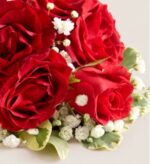 Close-up of a red rose corsage with white baby's breath flowers and variegated green leaves