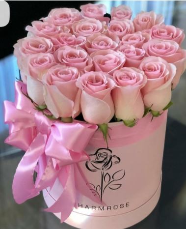 A luxurious circular pink gift box filled with fresh, light pink roses, decorated with a matching satin pink ribbon and bow.